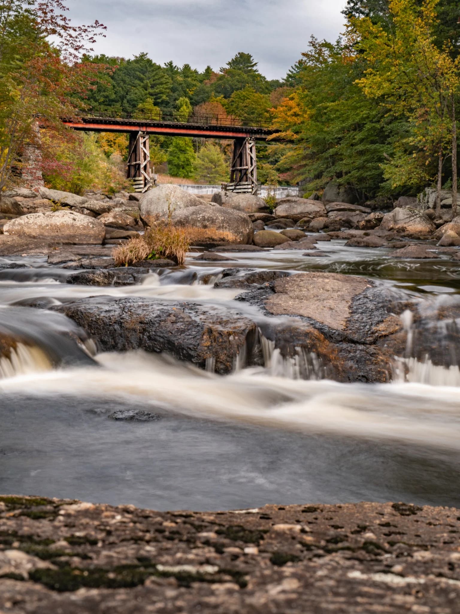 Autumn river and wooden bridge surrounded by granite boulders