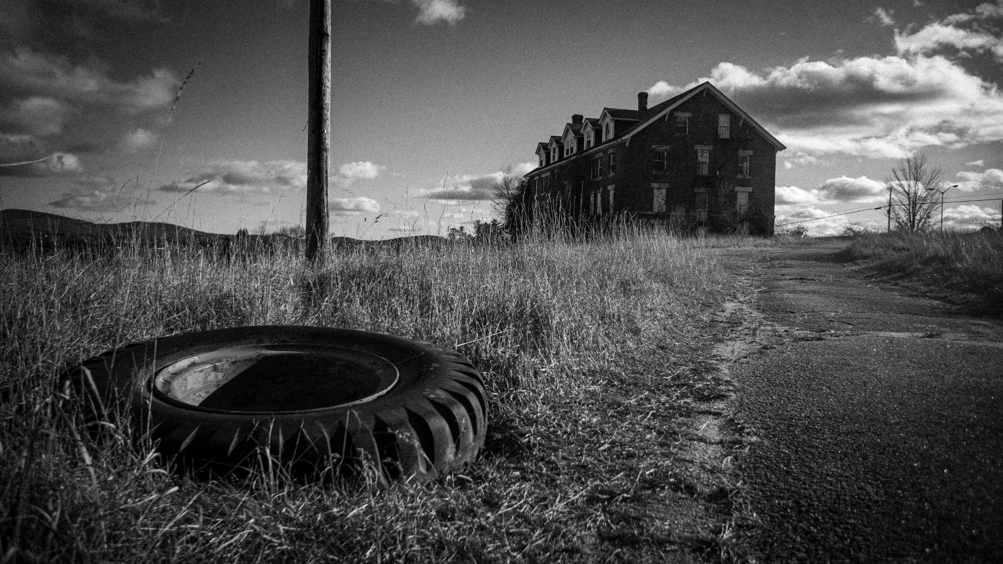 Black and white view of an abandoned building beyond a discarded tire